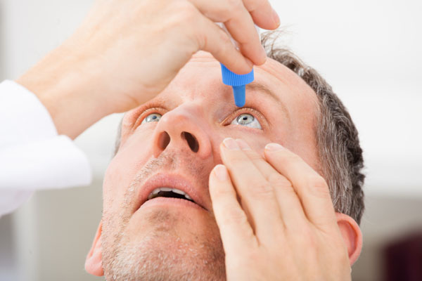 man putting eye drops in eyes due to poor indoor air quality in the winter