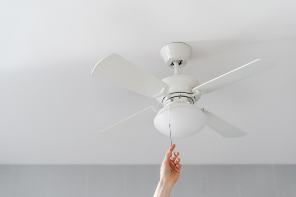 cropped view of a homeowner's hand turning on a ceiling fan for optimized indoor comfort