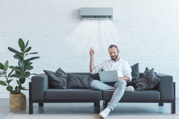 man working on his laptop on the couch while turning on ductless air conditioner