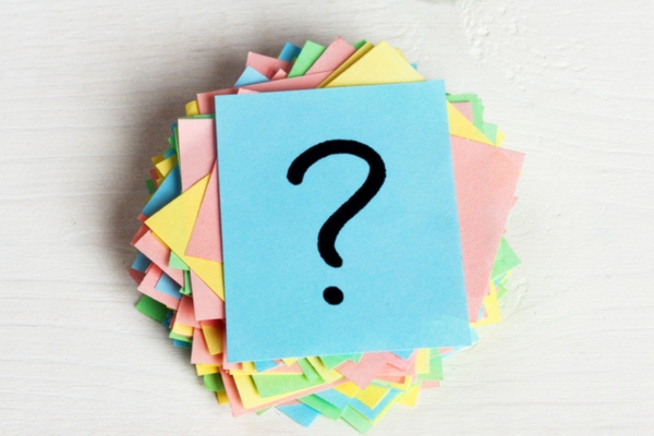 question mark on a stack of colored papers depicting FAQs about ducted vs ductless AC
